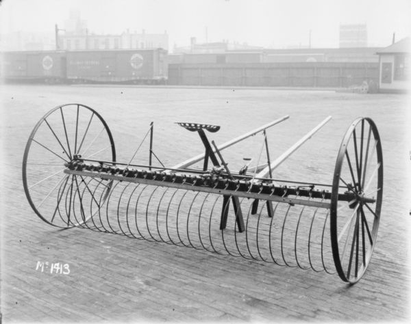 Dump Rake outdoors in a yard at McCormick Works. In the background are railroad cars, a tall, wooden fence, and buildings beyond.