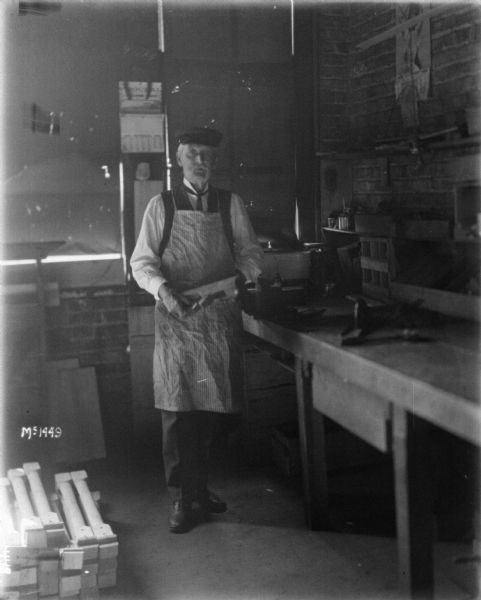 A man is posing with a finishing machine near a workbench in a factory building.