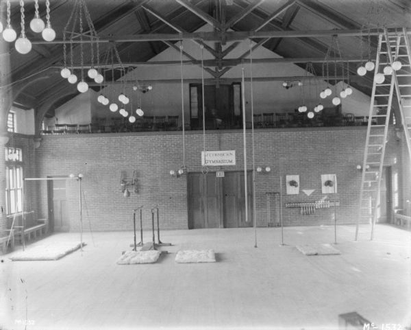 Interior, elevated view of McCormick's Gymnasium. Sports equipment is set up on the floor, and a punching bag is attached to the brick wall near a set of double doors. There is a balcony in the background lined with chairs.