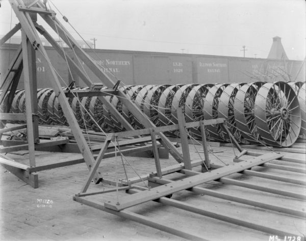 Sweep Rake outdoors at McCormick Works. There are wheels stacked in a row alongside the Sweep Rake on the right, and there are railroad cars in the background.