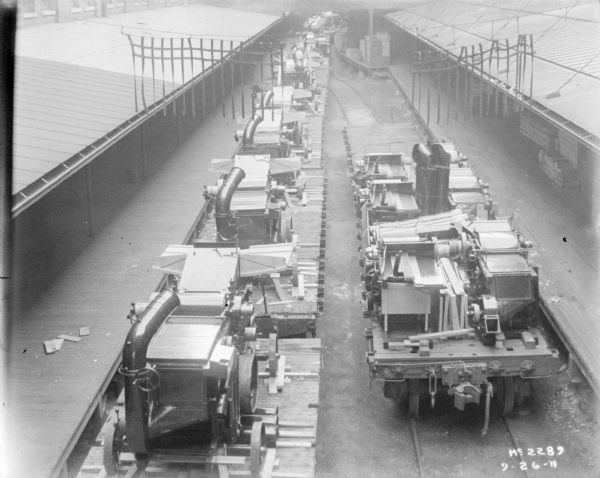 Elevated view of a line of threshers on flatbed railroad cars.