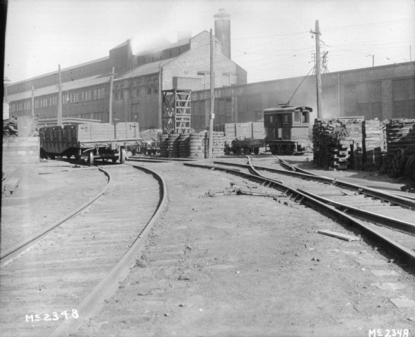 View down curving railroad tracks towards a railroad car, and factory buildings.