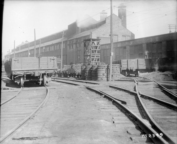 View down curving railroad tracks towards a railroad car, and factory buildings.
