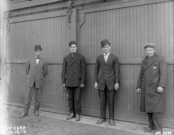 Group of men posing in front of the closed doors of a garage.