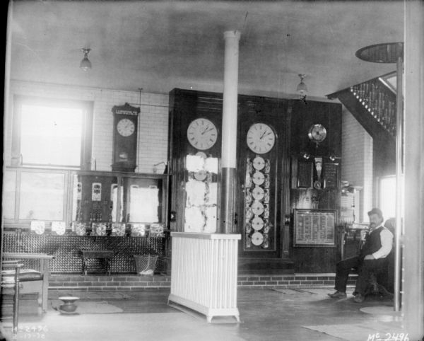 Time room inside McCormick Works. There is a male employee posing on the right near a large clock, a fireman's pole, and a flight of stairs.