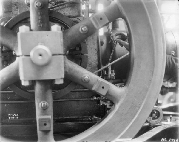 Close-up of a machine. A man's hand is holding a lever behind the gear or wheel in the foreground.