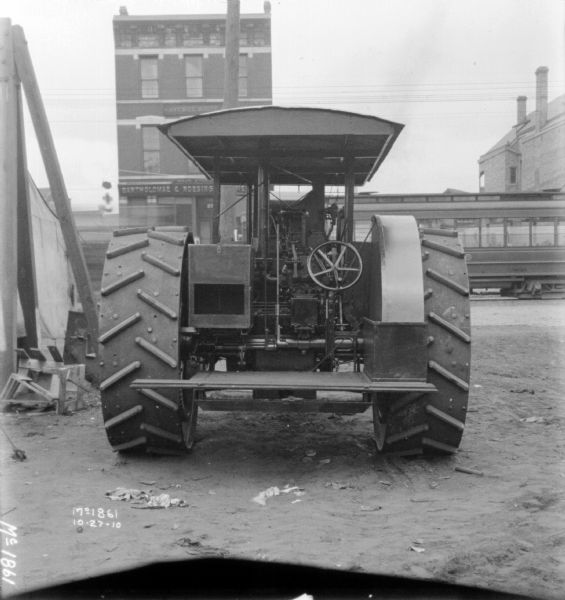 Rear view of a tractor parked in the yard at McCormick Works. In the background is a brick commercial building, with a sign that reads, in part: "Bartholomae & Roesing..." There is a streetcar moving along the street in front of the commercial buildings.