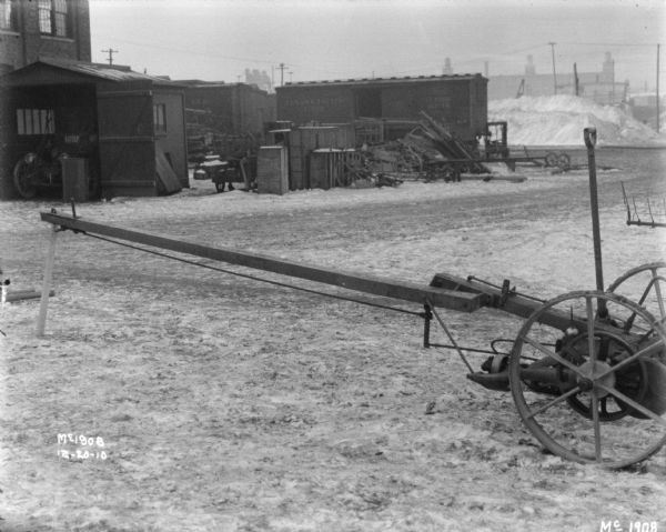 Mower outdoors in the yard at McCormick Works. Buildings and railroad cars are in the background.