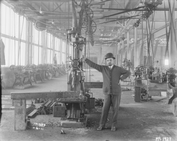 A man is posing with machinery in a manufacturing area.