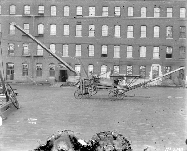 Thresher outdoors in the yard at McCormick Works. A brick factory building is in the background.