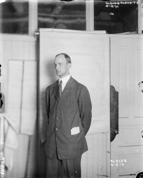 A man wearing a suit is standing indoors at McCormick Works. There is a white backdrop behind him, and an open door on the right.
