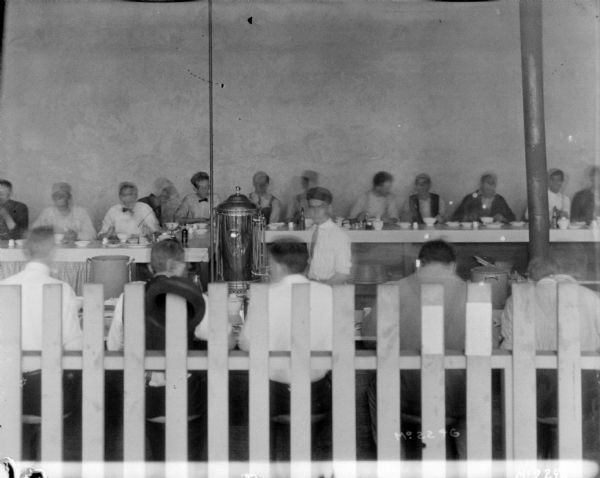 Employees eating in dining room at McCormick Works. There is a fence in the foreground.