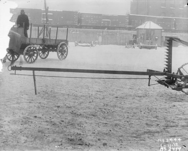 Mower Front Extension outdoors in the snowy yard at McCormick Works. There is a man in a horse-drawn wagon on the left. In the background are railroad cars on an elevated platform.