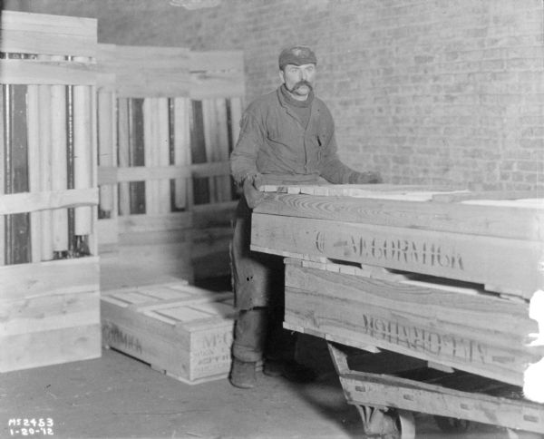 Male employee transporting machines crated for shipment on a cart. More crates are behind him.