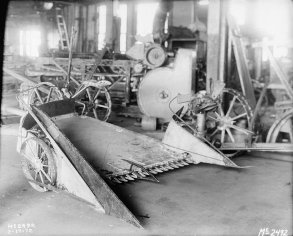 Reaper indoors in a factory building. Machinery and implements are in the background.
