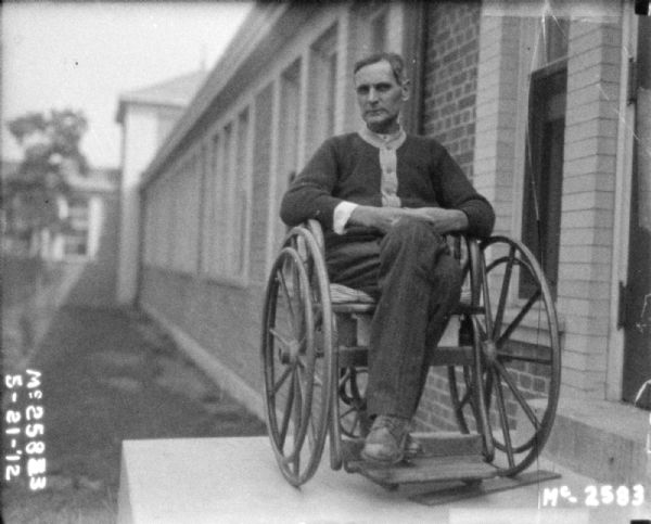 A man is sitting in a wheelchair on a platform near a doorway along the side of a building.