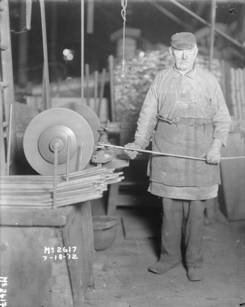 Man in work apron posing indoors at grinding (finishing) machine.