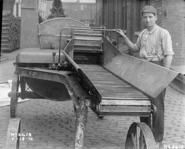 Employee posing with an Ensilage Cutter at McCormick Works. A man is sitting high up on a wagon in the background.