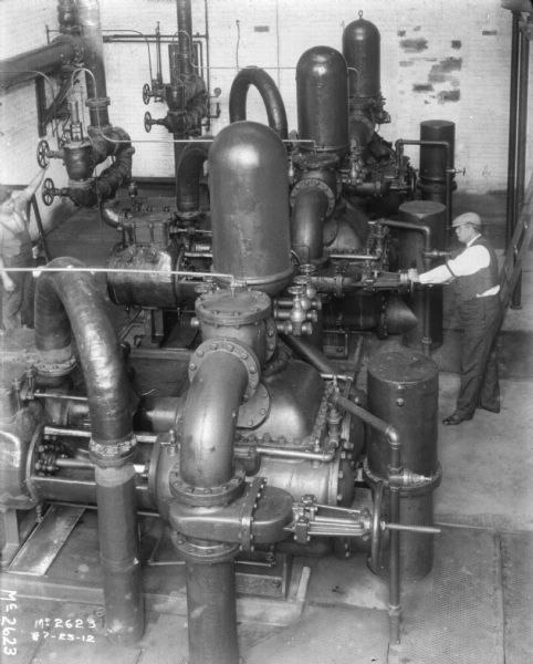Elevated view of two men working in a boiler room.