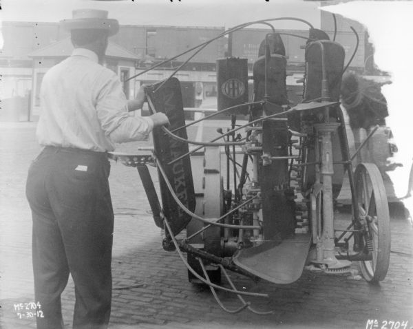 Man demonstrating parts which fold up on Corn Binder outdoors in the yard at McCormick Works. In the background are railroad cars on an elevated platform.