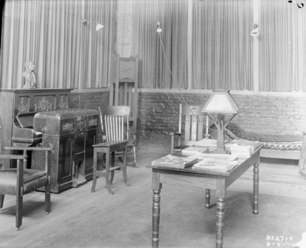 Employee lounge in the McCormick Works Club House. There is a piano on the left, a clock in the corner, and tables and chairs.