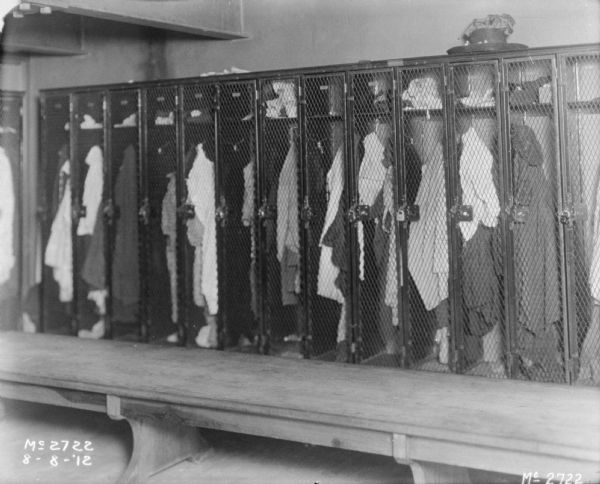 Clothes are hanging in employee lockers. A long wooden bench is in the foreground.