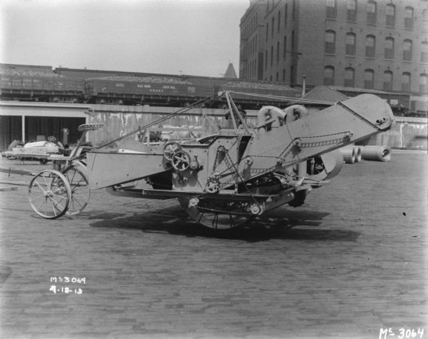 Corn Binder outdoors in the yard. In the background are railroad cars on an elevated platform, with brick buildings beyond.