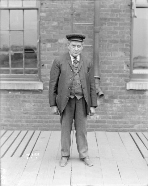 Full-length portrait of a man standing on a loading dock in front of a brick wall.