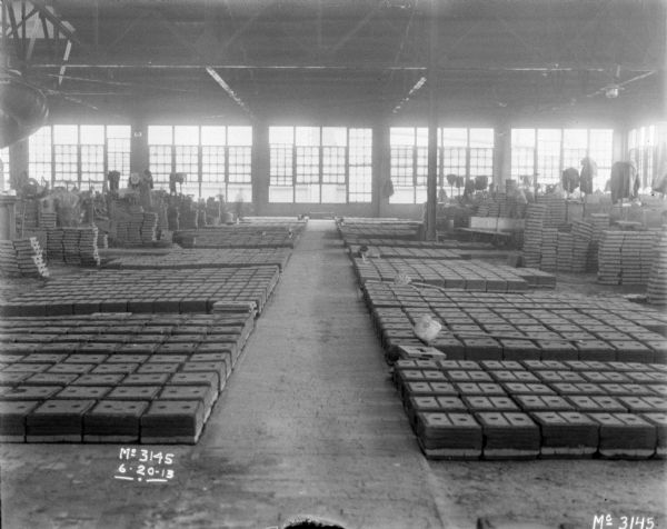 Interior view of the forging area in the factory. Men are working in the background. There are windows all along the back wall.