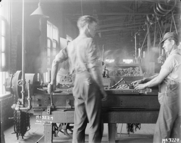 Two men are guiding parts into a machine at McCormick Works.