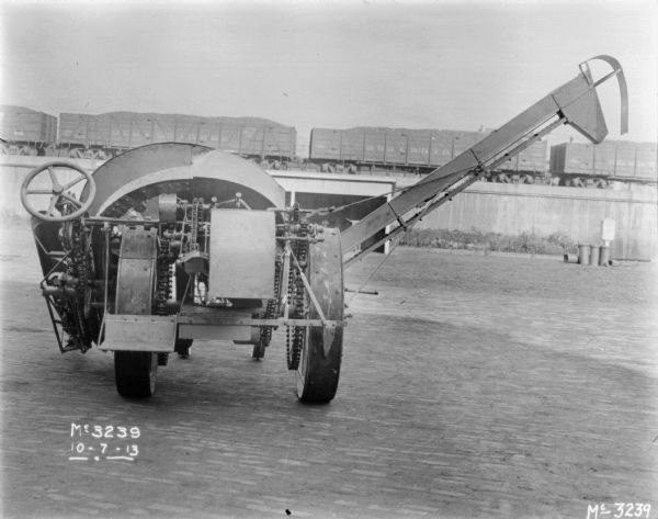 Rear view of a Corn Binder outdoors in the yard. Railroad cars on an elevated platform are in the background.