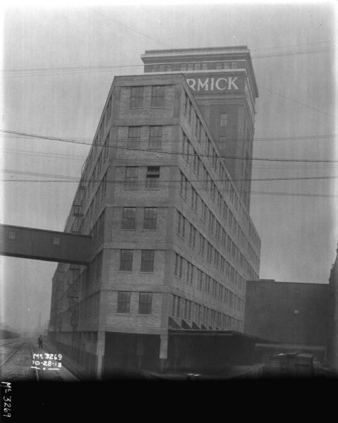 View looking up at a building under construction. The new tower above the building has a sign that reads: "McCormick." There is a man standing near railroad tracks on the left.