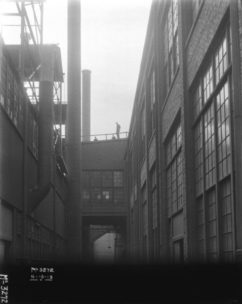 View looking up at factory buildings. Men are standing on the roof.
