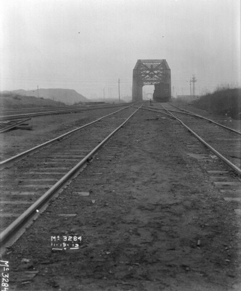 View between two sets of railroad tracks towards a metal railroad bridge.