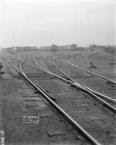 View down multiple sets of railroad tracks, towards railroad cars in a railyard.