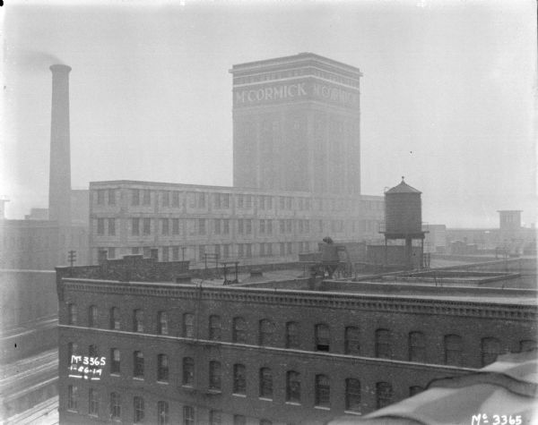 View from roof looking over factory buildings at McCormick Works. An addition on the top of one building has a sign near the roof that reads: "McCormick." There is a smokestack in the background on the left.