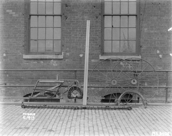 A Dump Rake, dismantled for shipping, set up along a railing. There is a brick factory wall in the background.