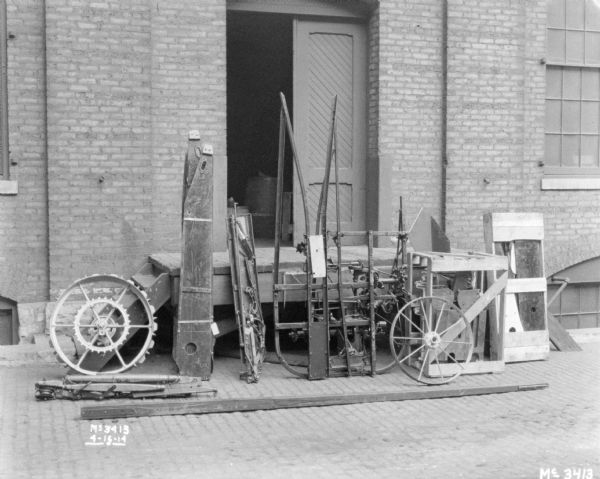 A Binder dismantled for shipping, set up along wood steps leading to a double door of a brick factory building.
