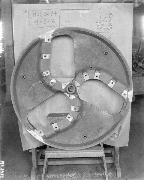 Interior blade of ensilage cutter. A board behind the blade has part numbers written on it.