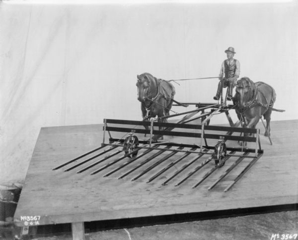 Model of a Hay Stacker, with a miniature man with horse, on a table. There is a backdrop behind.