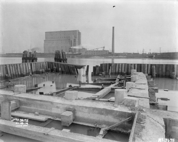 View of river from docks. Industrial buildings and a smokestack are on the far shoreline.