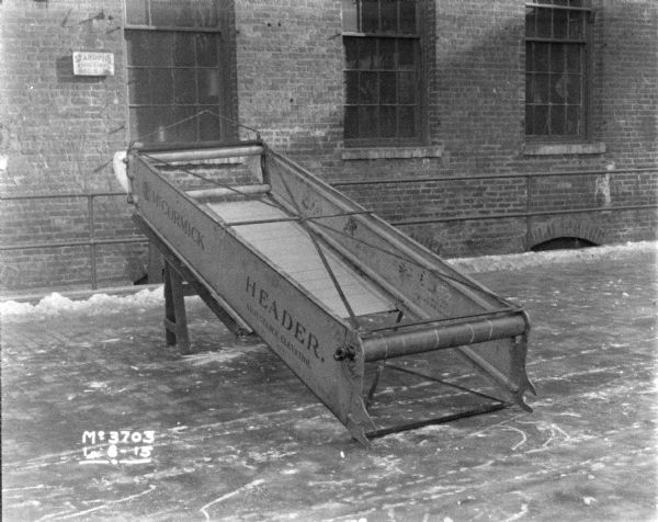 McCormick Header binder, showing parts and conveyor, set-up outdoors in the factory yard. There is a brick factory building in the background.