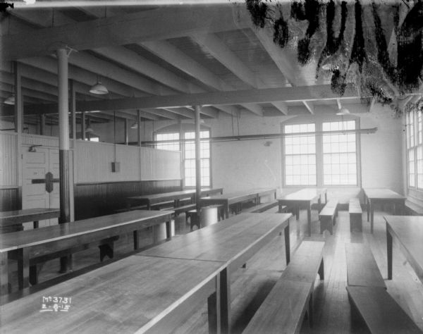 View of an employee dining room, with long tables and benches. The ceiling rafters are exposed, and large windows are along the walls.