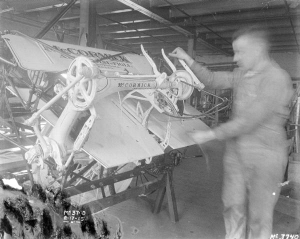 View of a man, blurred from motion, feeding twine through binder mechanism inside a factory.