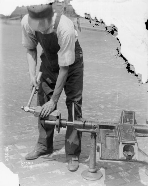 Man working on mower with a hammer outdoors in the yard at McCormick Works.