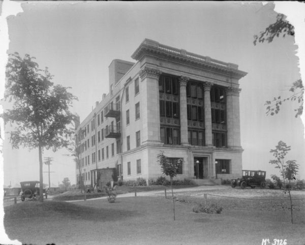 Exterior view of the Fresh Air Hospital. Automobiles are parked near the building. Chairs are outdoors on the lawn in front of the building.