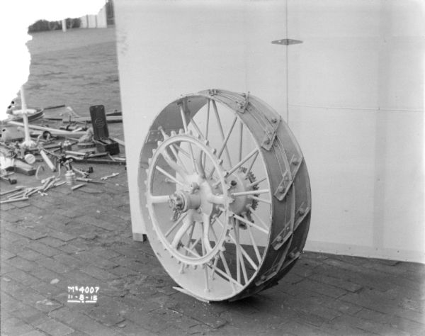 Wheel set-up outdoors on the cobblestones in factory yard. There is a backdrop behind. Other parts are lying on the ground on the left behind the backdrop.
