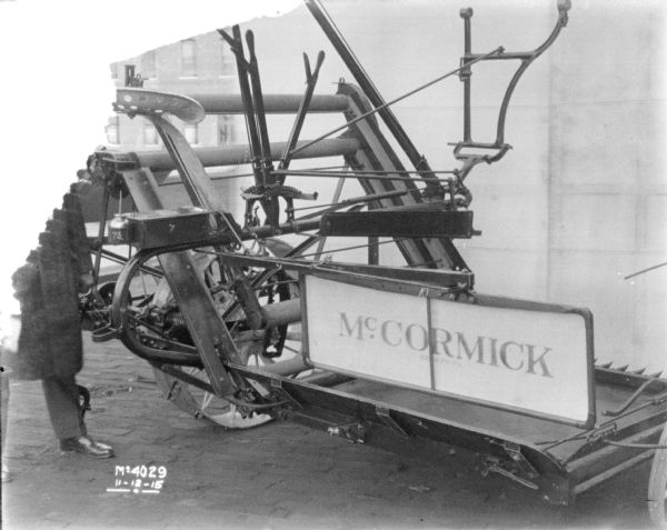 A man (face obscured) is standing next to a McCormick Binder in front of a backdrop outdoors in the factory yard.