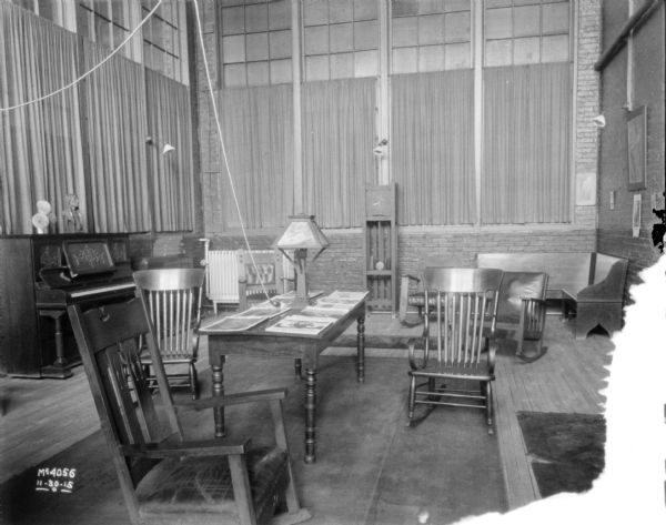 Tables and chairs are in the foreground. A piano is along the left wall in the background, and a clock is against the far wall. The tall windows have been partially curtained. 
