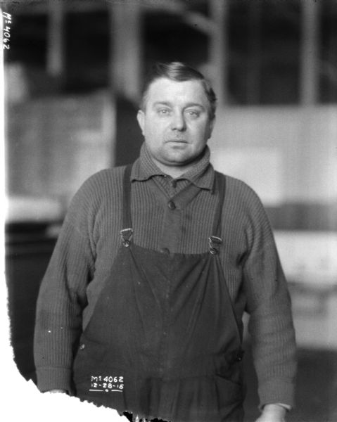 Three-quarter length portrait of a man indoors at McCormick Works. He is wearing a sweater and overalls.